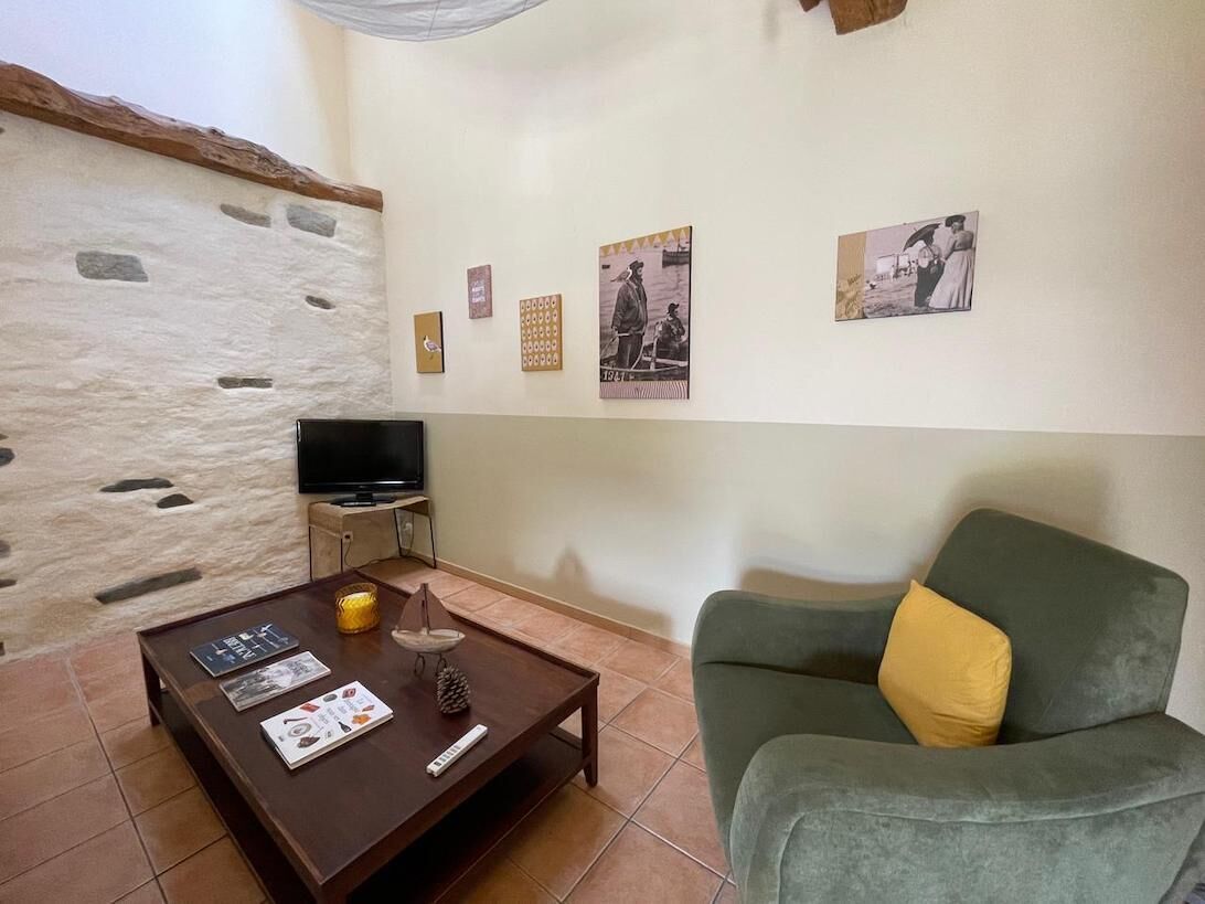 A living room with a stone wall, a television, a coffee table with magazines, and a green sofa with a yellow pillow.