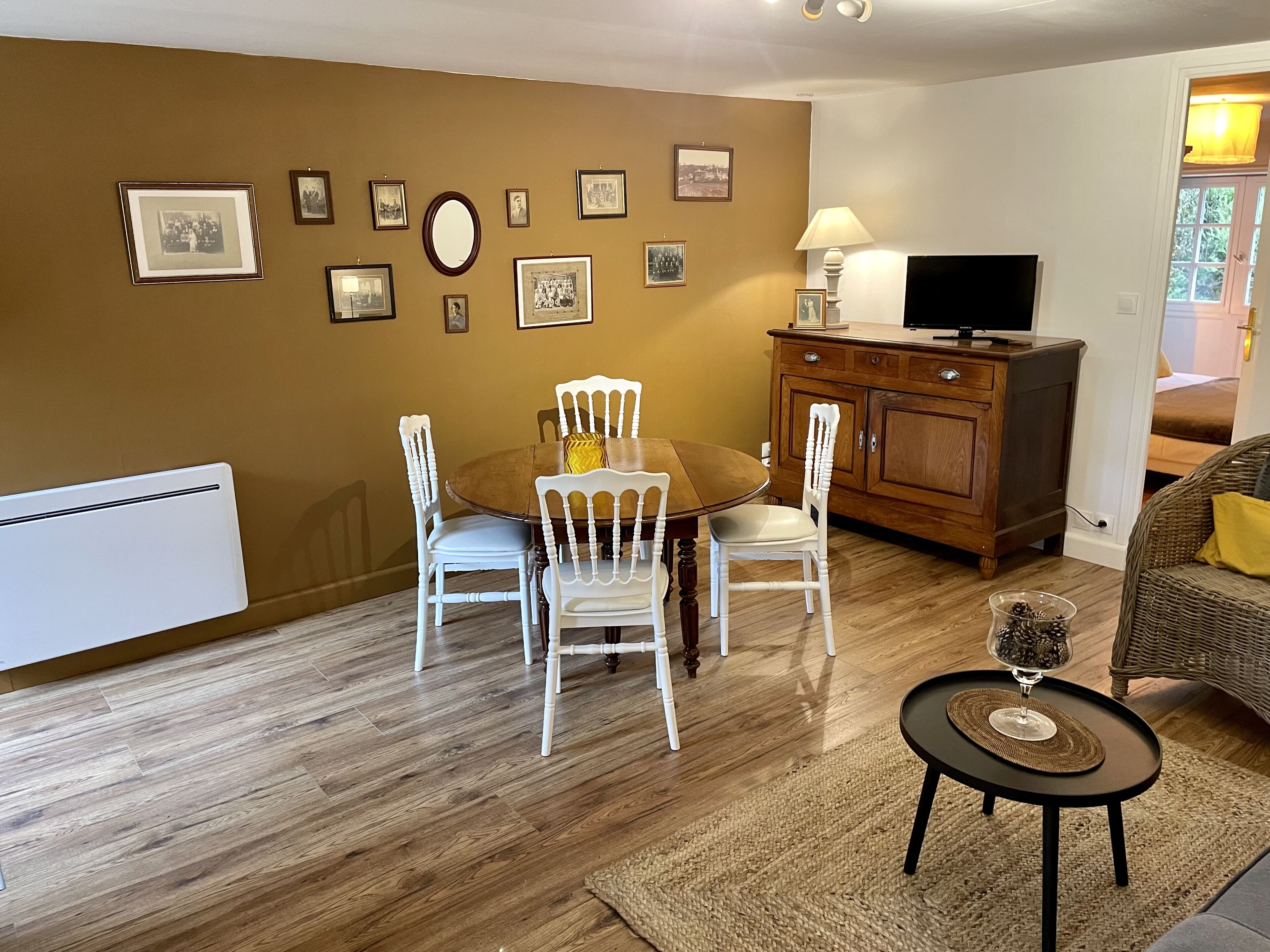 A dining area with a wooden table and white chairs, a television on a cabinet, and framed pictures on the wall.