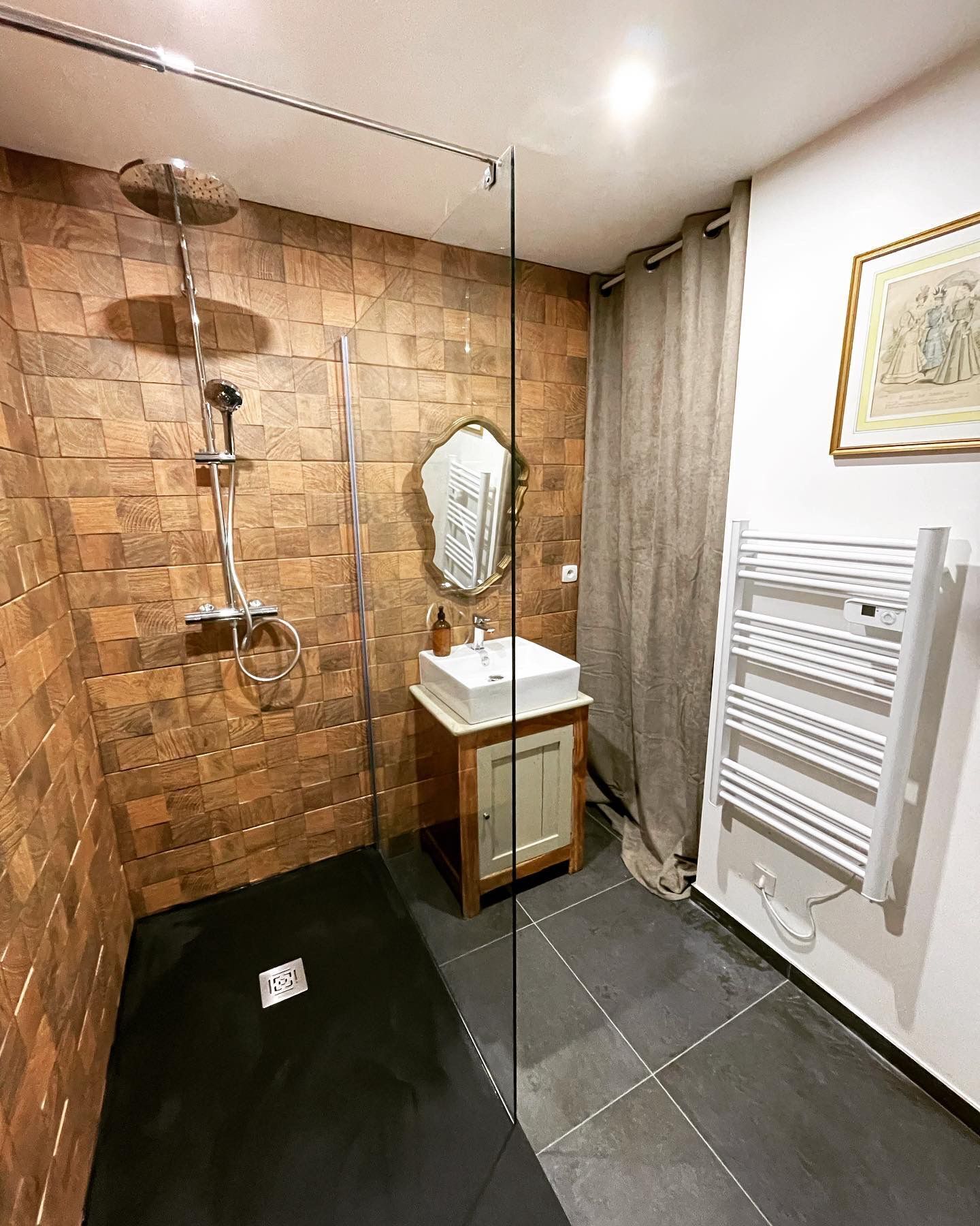 Un baño con cabina de ducha de vidrio, revestimiento de madera en la pared, un mueble de madera con espejo y un radiador blanco.