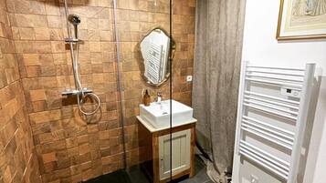 Un baño con cabina de ducha de vidrio, revestimiento de madera en la pared, un mueble de madera con espejo y un radiador blanco.