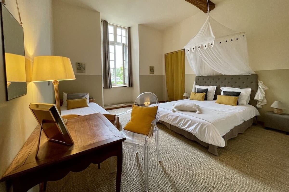 Een slaapkamer met een bed, nachtkastje, lamp en een stoel.