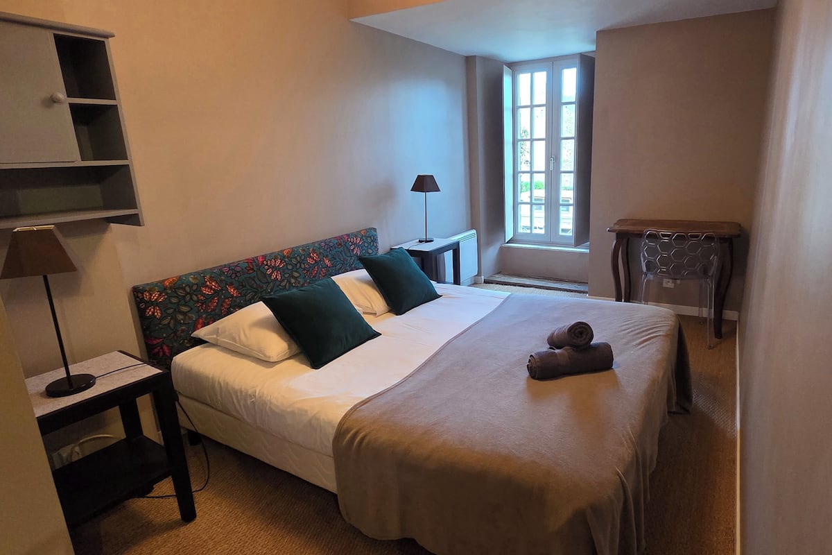 Een netjes ingerichte hotelkamer met een bed, nachtkastjes, een lamp en een raam met uitzicht.
