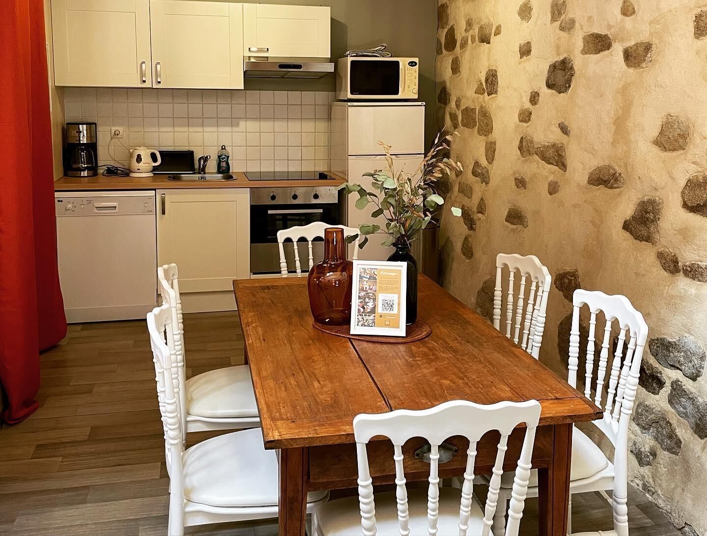 Una cocina compacta con armarios blancos, microondas, cafetera y lavavajillas.