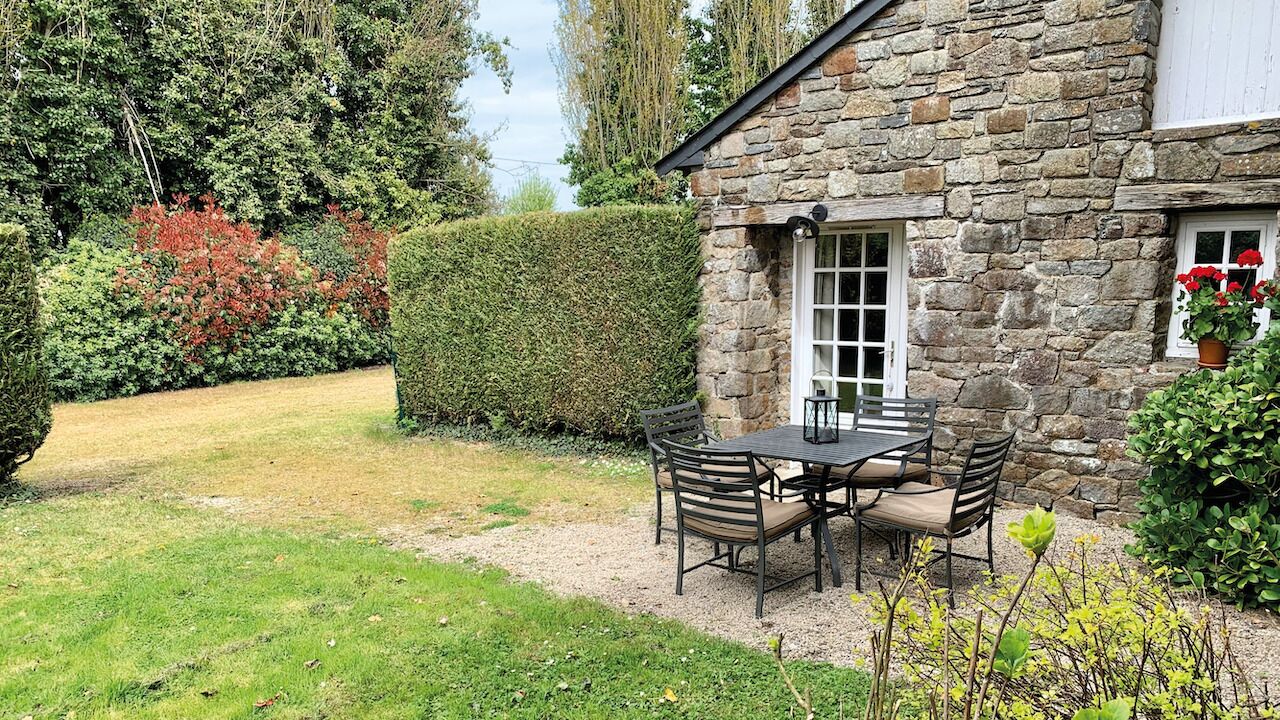 Un bâtiment en pierre doté d’un patio avec jardin, comprenant une table et des chaises.