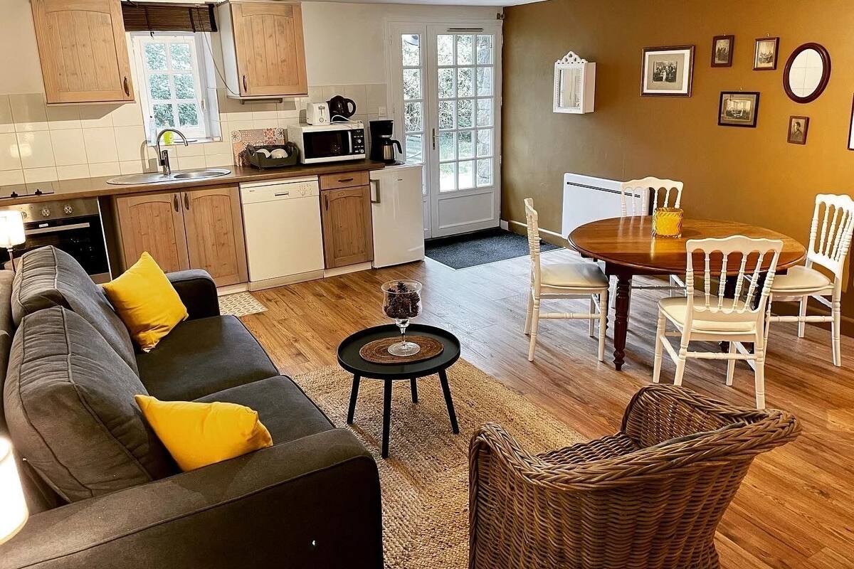 Een moderne keuken met houten kastjes, een eetgedeelte met een ronde tafel en witte stoelen, en een woonkamer met een bank en salontafel.