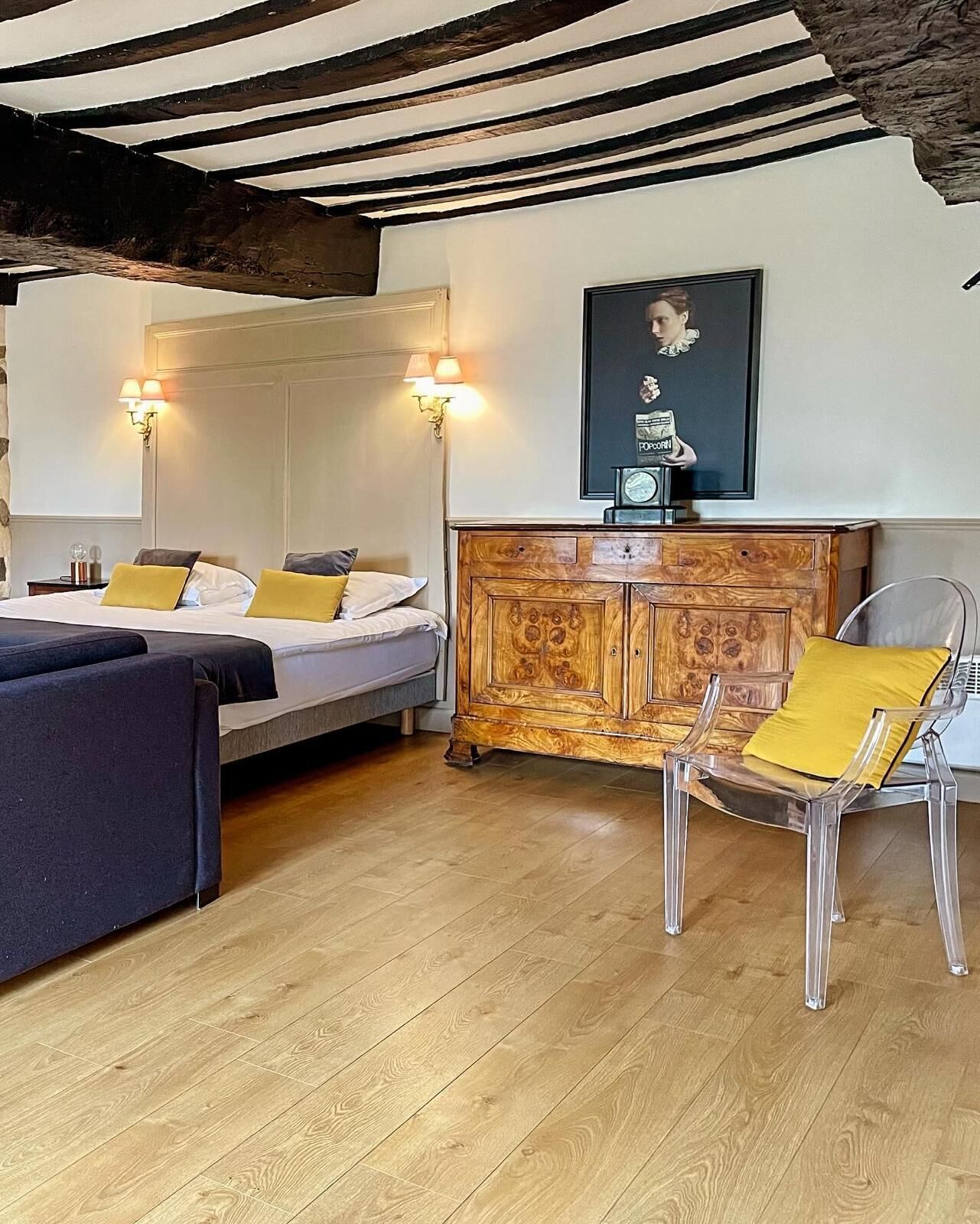 A room with a bed, a sofa, a wooden cabinet, and a chair. There are wall sconces and a framed picture on the wall.