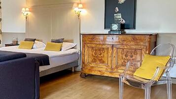 A room with a bed, a sofa, a wooden cabinet, and a chair. There are wall sconces and a framed picture on the wall.