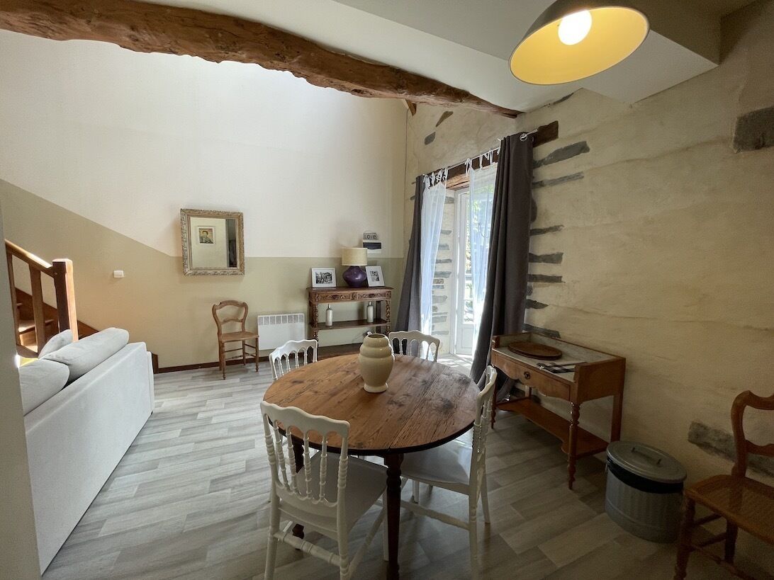Un salon chaleureux avec une table à manger en bois, des chaises blanches, un canapé et un escalier menant à l’étage.