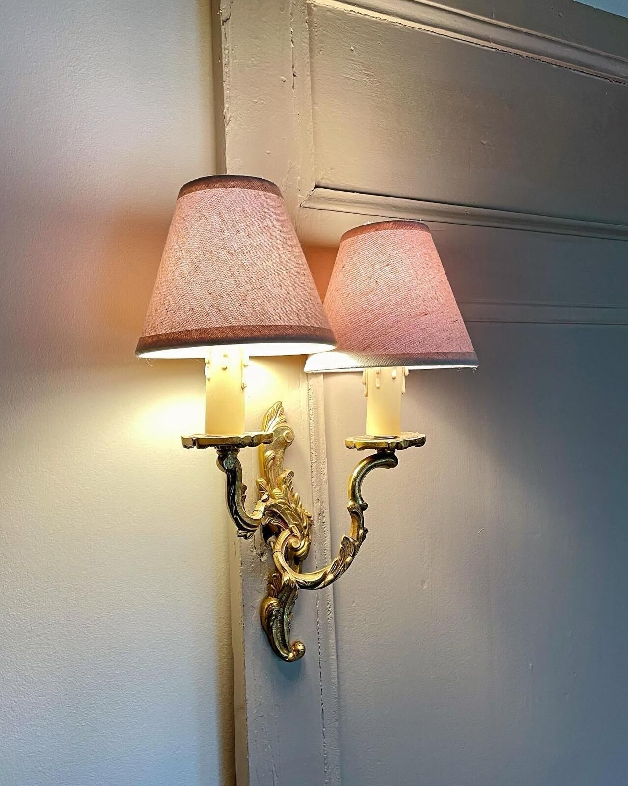 Een wandlamp met twee lampenkappen, een decoratieve metalen voet en een witte muur.