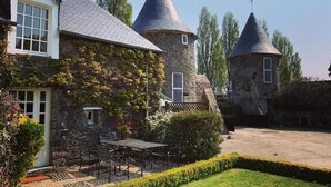 A stone building with ivy, a garden with a table and chairs, and two conical towers.