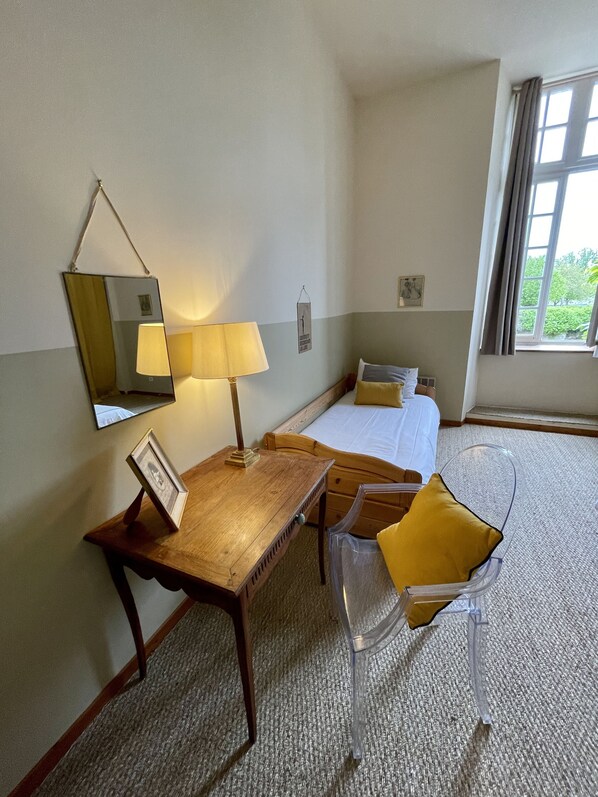 Una habitación de hotel con un escritorio de madera, una silla, una cama y un ventanal con cortinas.