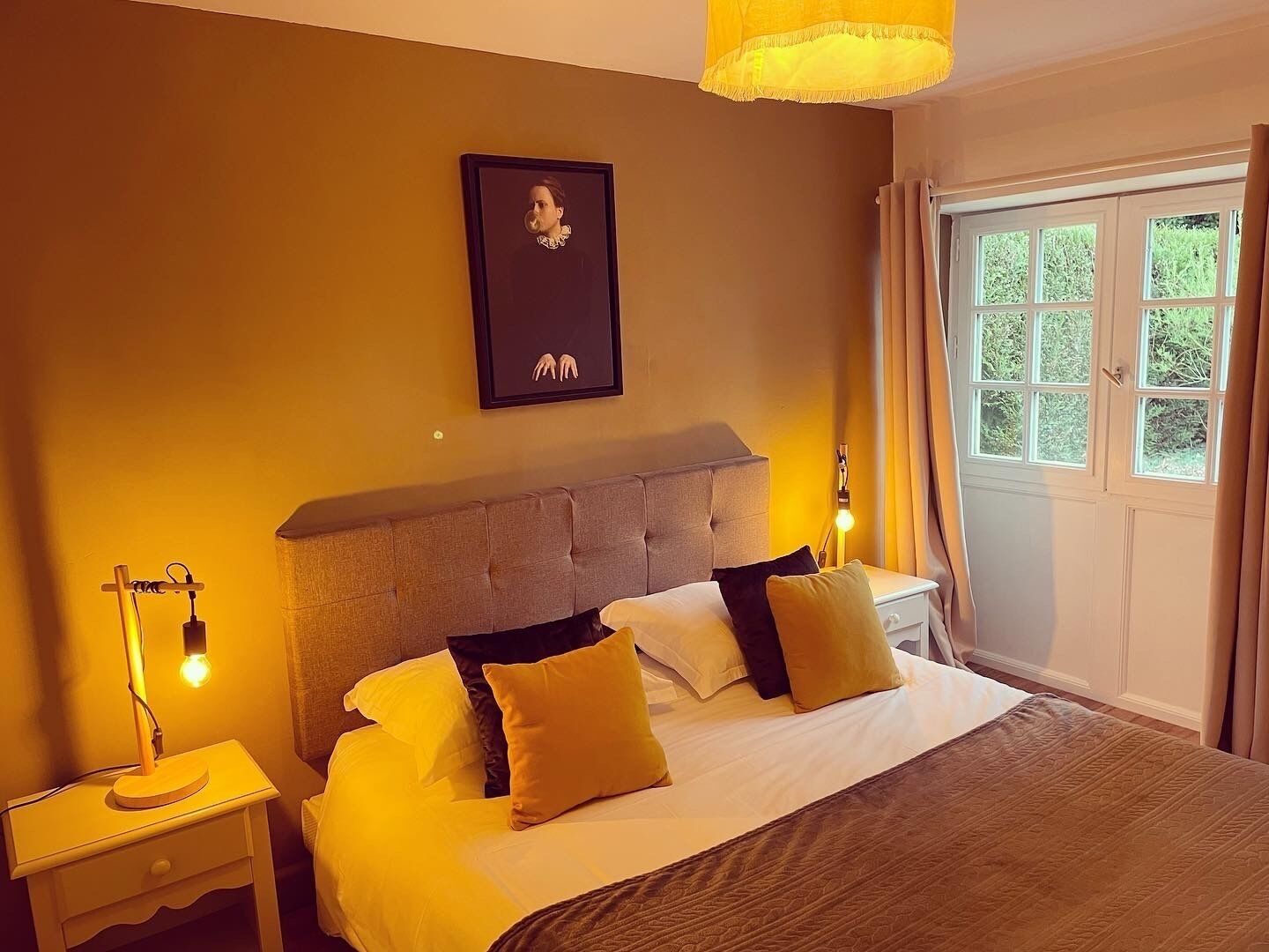 A bedroom with a bed, nightstands, a lamp, a framed picture, and a window with curtains.