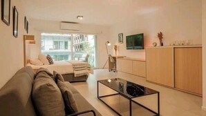 Una sala moderna con un sofá, una mesa de centro y un televisor. Cuenta con una cocina con armarios y una encimera.