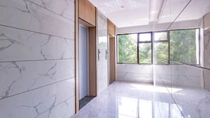 A modern interior with marble walls, a wooden door, and a large window with a view of greenery. - Maya 3-bed Apartment in Nairobi (Nairobi)