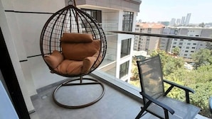 A balcony with a hanging chair, a table, and a chair. - Maya 3-bed Apartment in Nairobi (Nairobi)