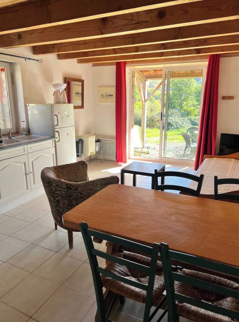 A cozy room with a wooden table and chairs, a small kitchenette, and a window with a view of greenery.