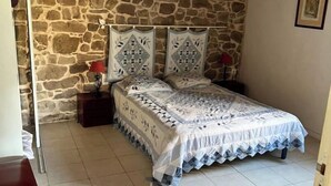 Ein Schlafzimmer mit Stehwänden, einem Bett mit gemustertem Überwurf, einem Nachttisch mit Lampe und einer Holzbank.