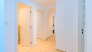 Un pasillo con paredes blancas y suelo de baldosas que conduce a un baño con inodoro.