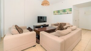 Una sala de estar con dos sofás color beige, una mesa de centro de madera, un televisor de pantalla plana y una araña.