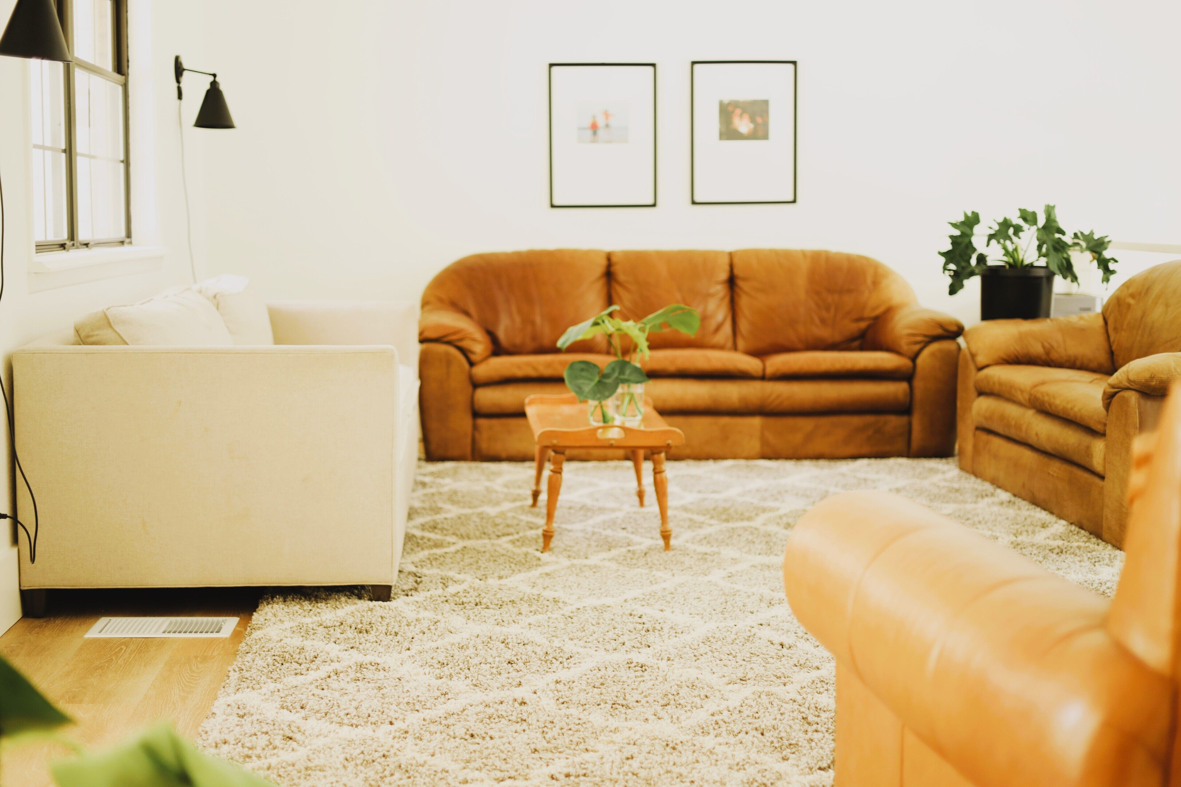 Ein Wohnzimmer mit einem beigen Sofa, einem braunen Ledersessel, einem kleinen Holztisch mit einer Pflanze und einem weißen Teppich.