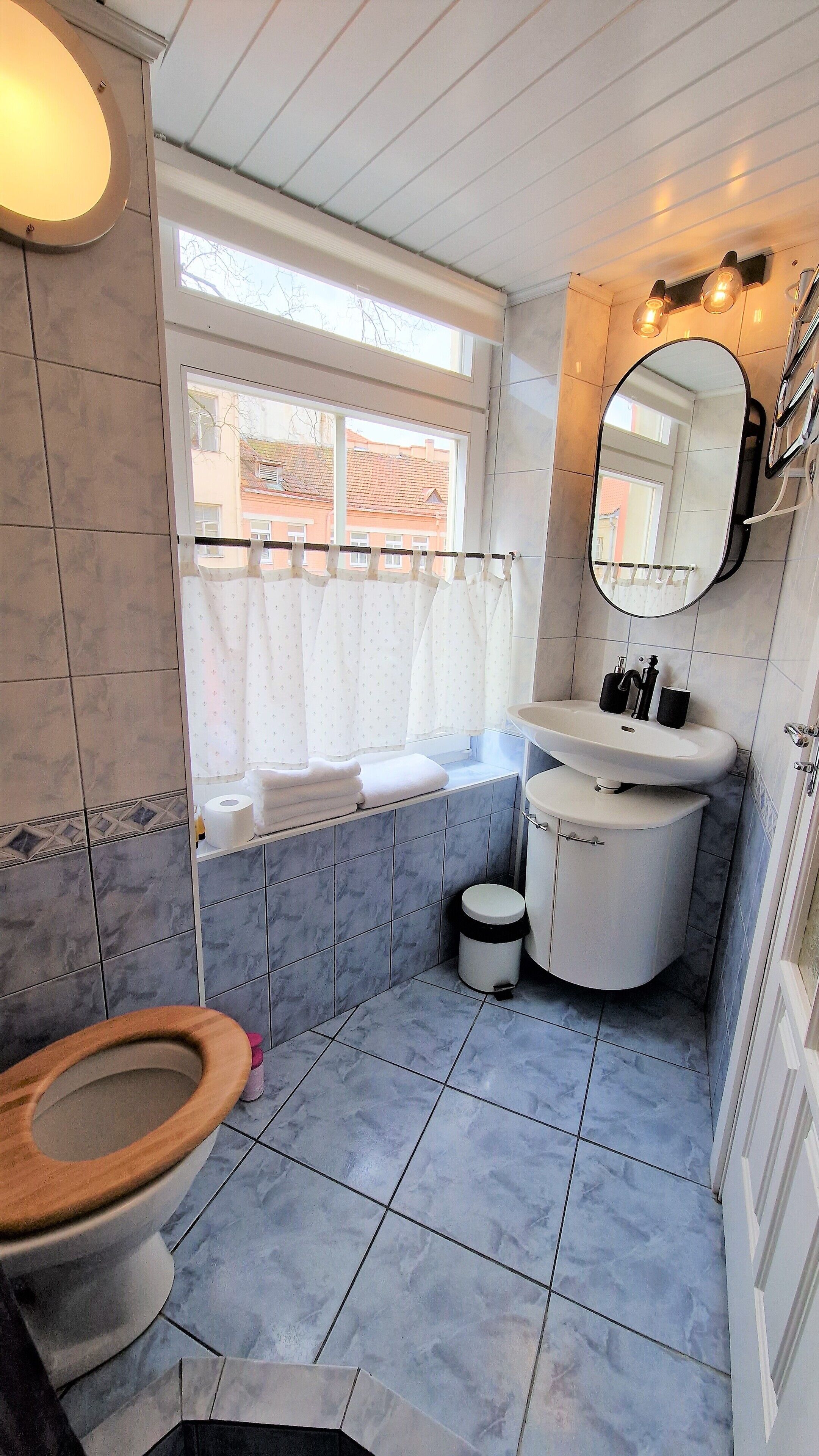 A bathroom with a toilet, sink, and window with curtains.