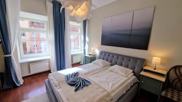 A bedroom with a bed, a nightstand, a lamp, a window with curtains, and a painting on the wall.