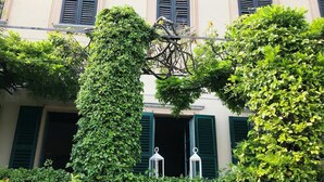 A building with multiple windows and green shutters, surrounded by lush greenery and two white lanterns on the windowsill. - Palazzo Rosati 1701 – An 18th-Century Palace with a Stunning View over Lake Como (Bonzanigo)