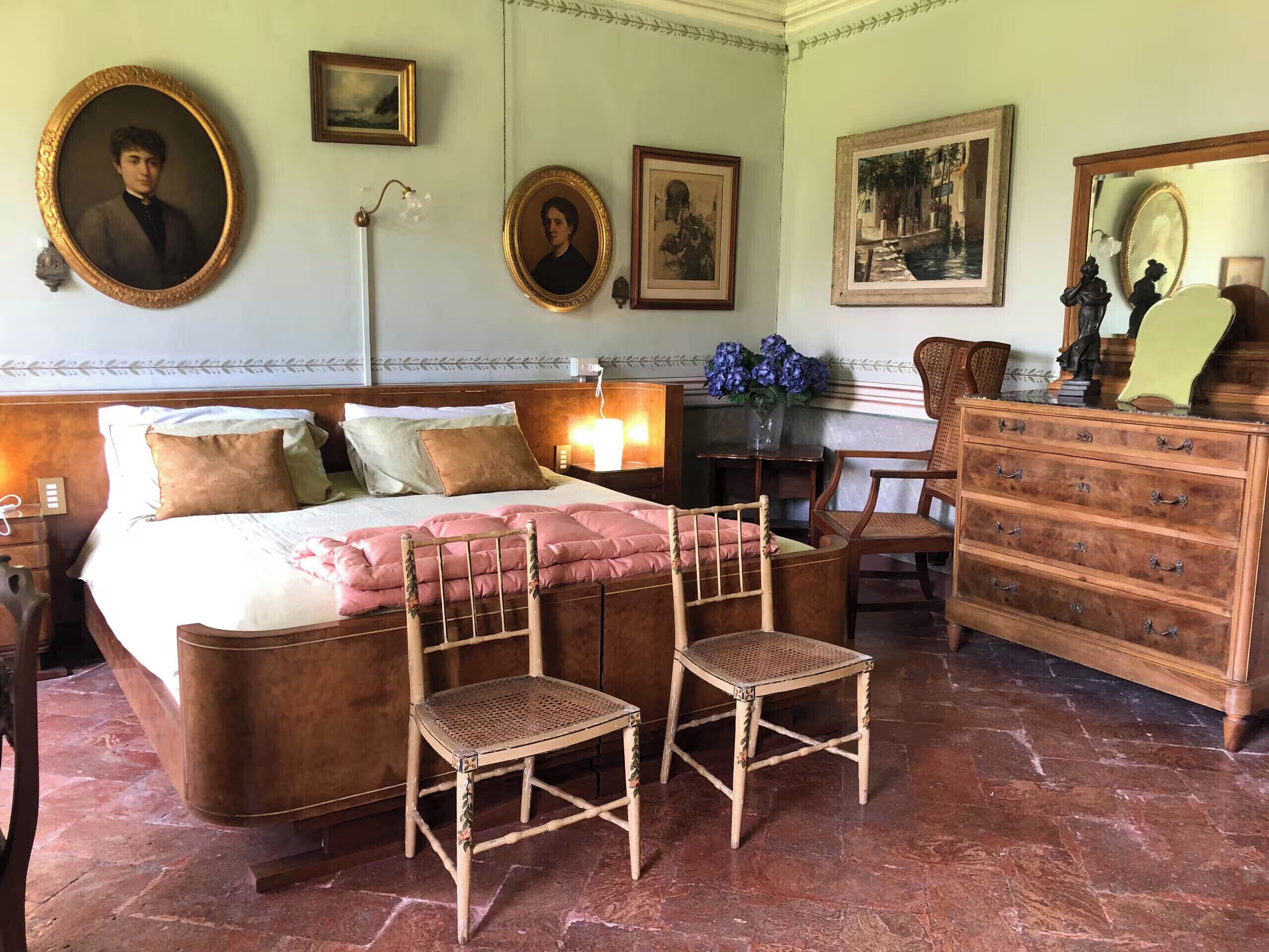Een slaapkamer met een bed, twee stoelen, een dressoir en foto's aan de muur.