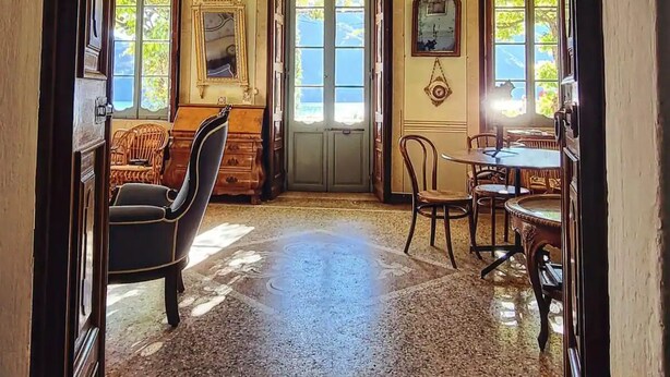 A grand hallway with a detailed fresco ceiling, a wooden door, and a dining area with chairs and tables. - Palazzo Rosati 1701 – An 18th-Century Palace with a Stunning View over Lake Como (Bonzanigo)