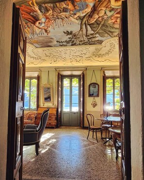Un amplio pasillo con un techo decorado con frescos, una puerta de madera y un comedor con sillas y mesas.