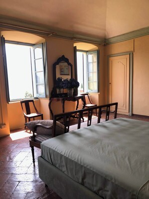 A bedroom with a bed, a chair, a table, and a window with curtains. - Palazzo Rosati 1701 – An 18th-Century Palace with a Stunning View over Lake Como (Bonzanigo)