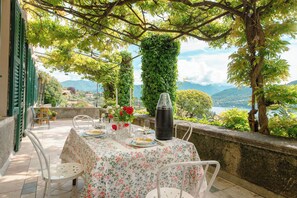 Un área de comedor al aire libre con una mesa lista para dos personas, rodeada de follaje y con vistas a un paisaje montañoso.
