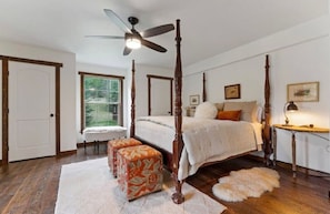A four-poster bed in a bedroom with a ceiling fan, a window, and a door.