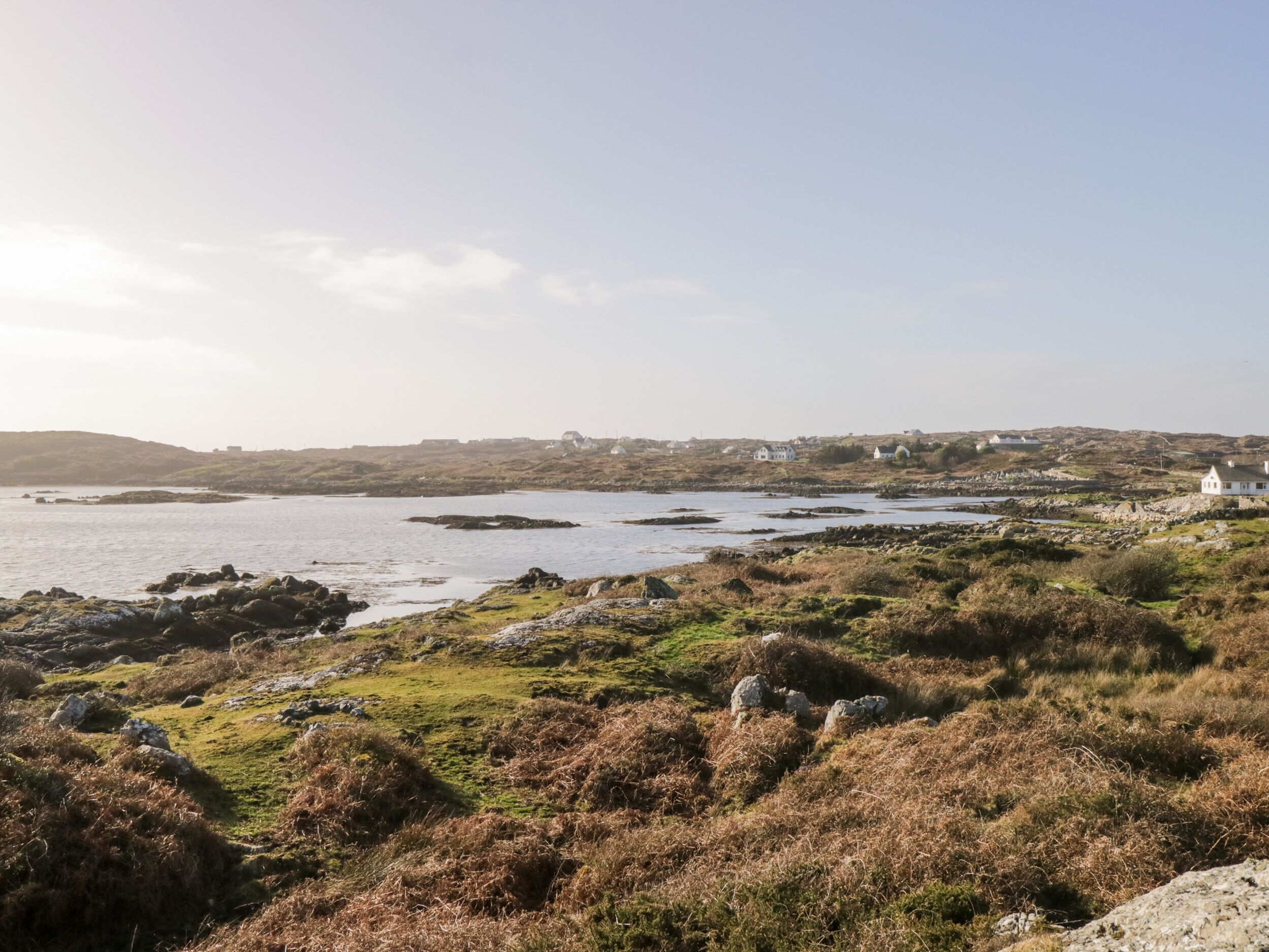 A coastal landscape with rocky terrain, grassy areas, and scattered white buildings.