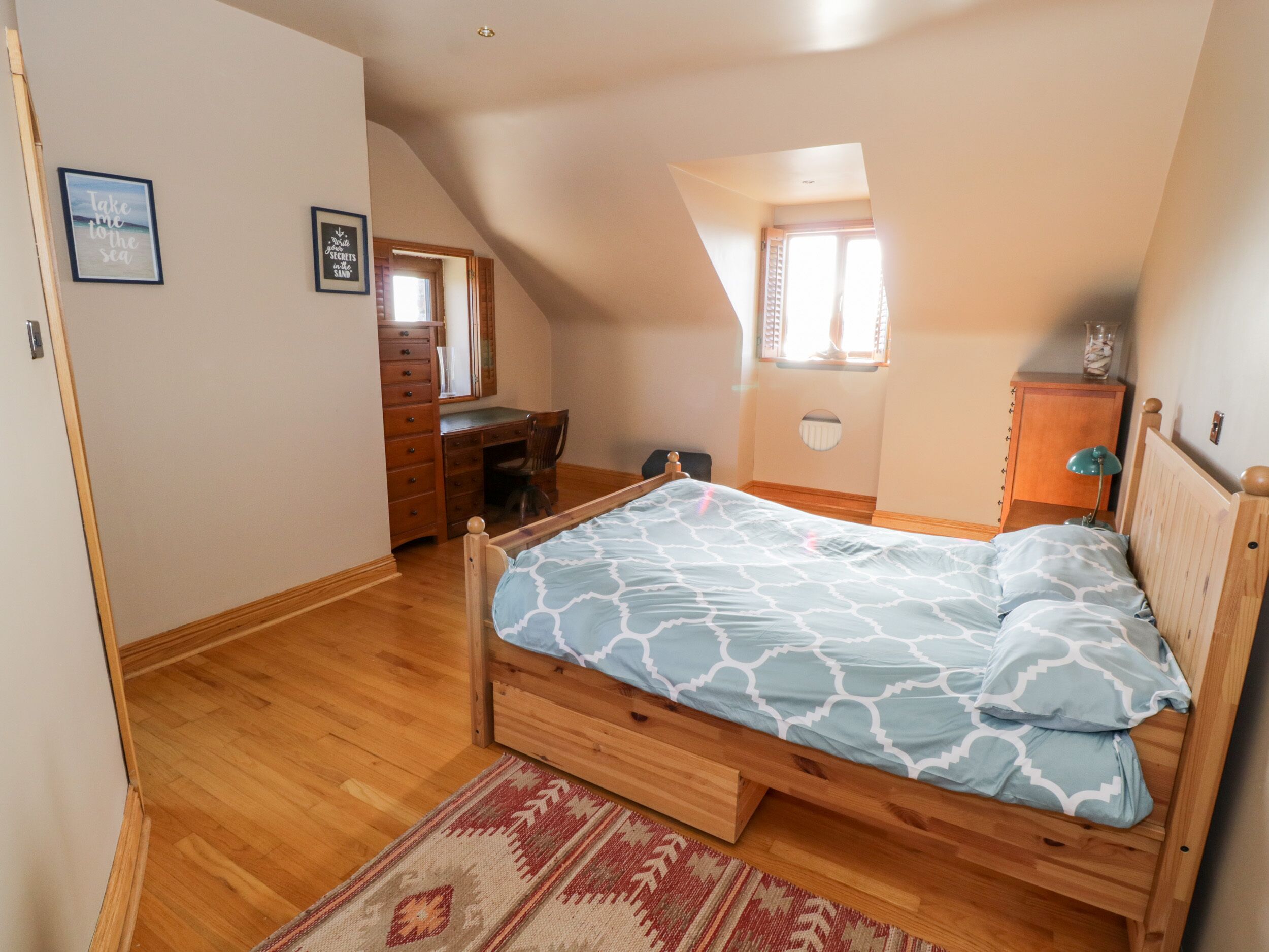 Un dormitorio con una cama de madera, un aparador, un escritorio y una ventana que ofrece vistas al cielo.