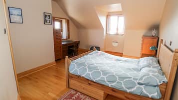 Un dormitorio con una cama de madera, un aparador, un escritorio y una ventana que ofrece vistas al cielo.