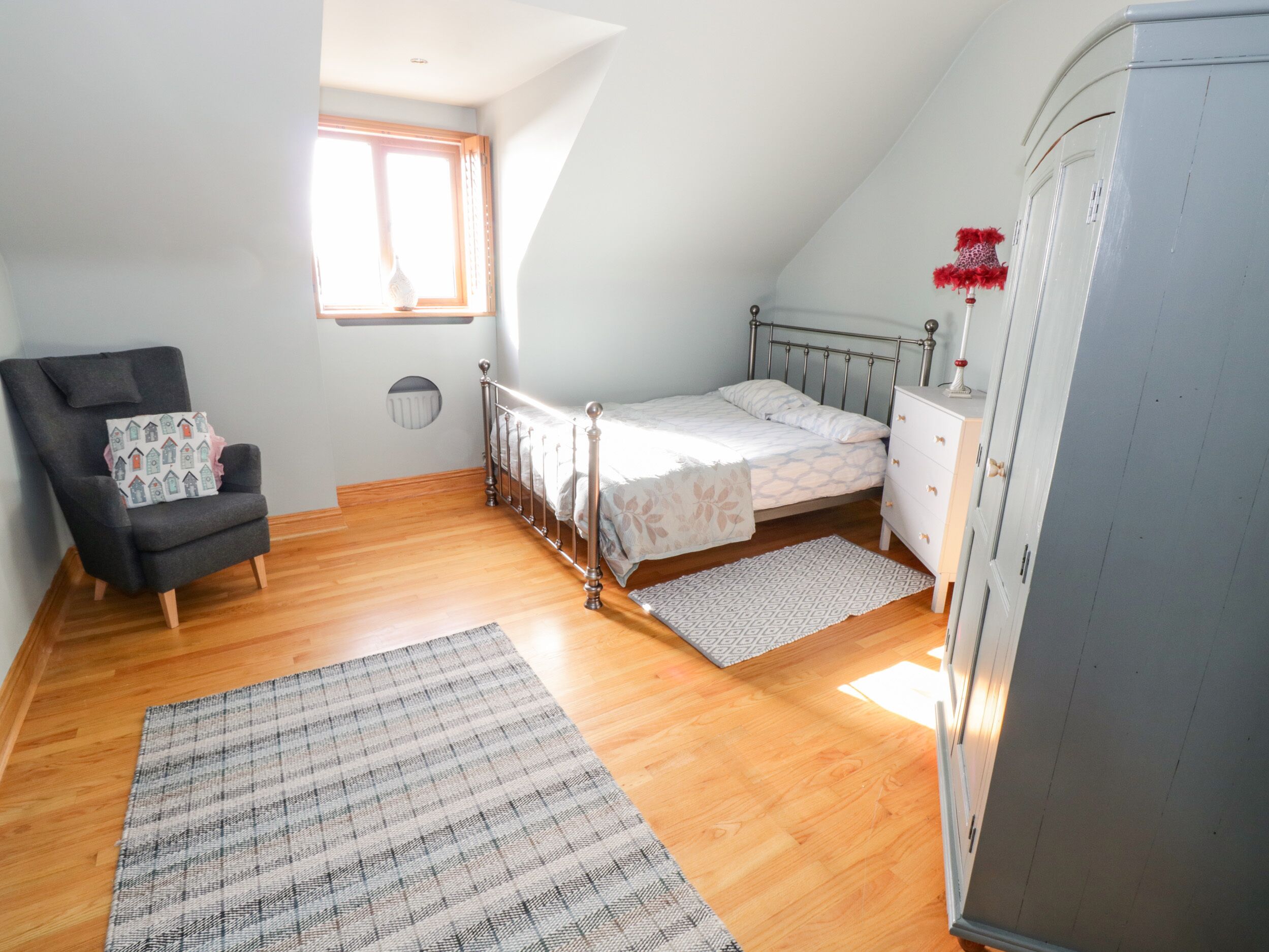 A bedroom with a bed, a chair, a wardrobe, and a window.
