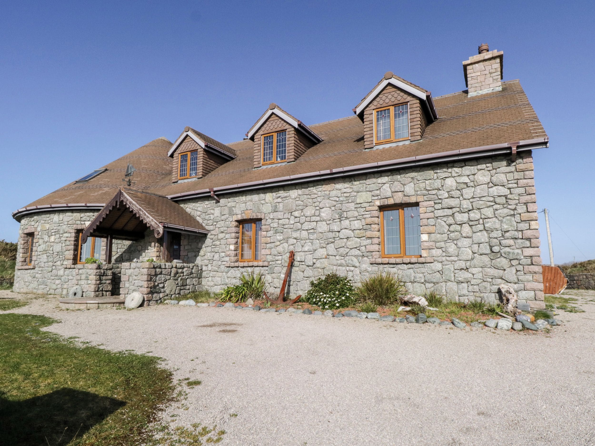 Une maison en pierre avec un toit à deux versants, de nombreuses fenêtres et une allée gravillonnée.
