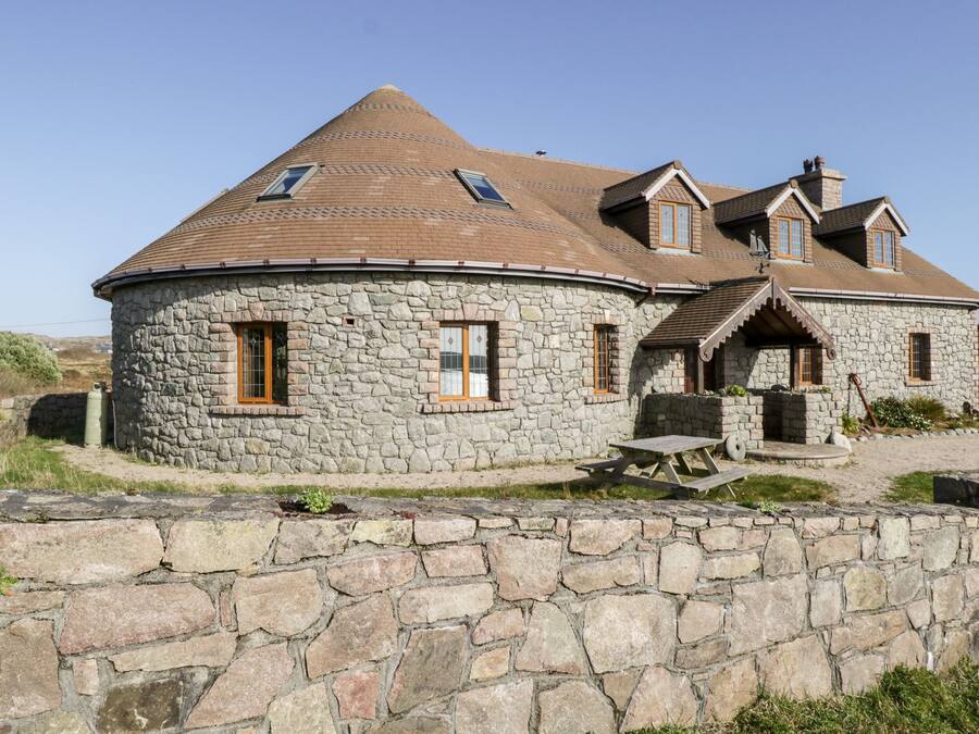 A stone house with a rounded roof, multiple windows, and a stone wall in front.