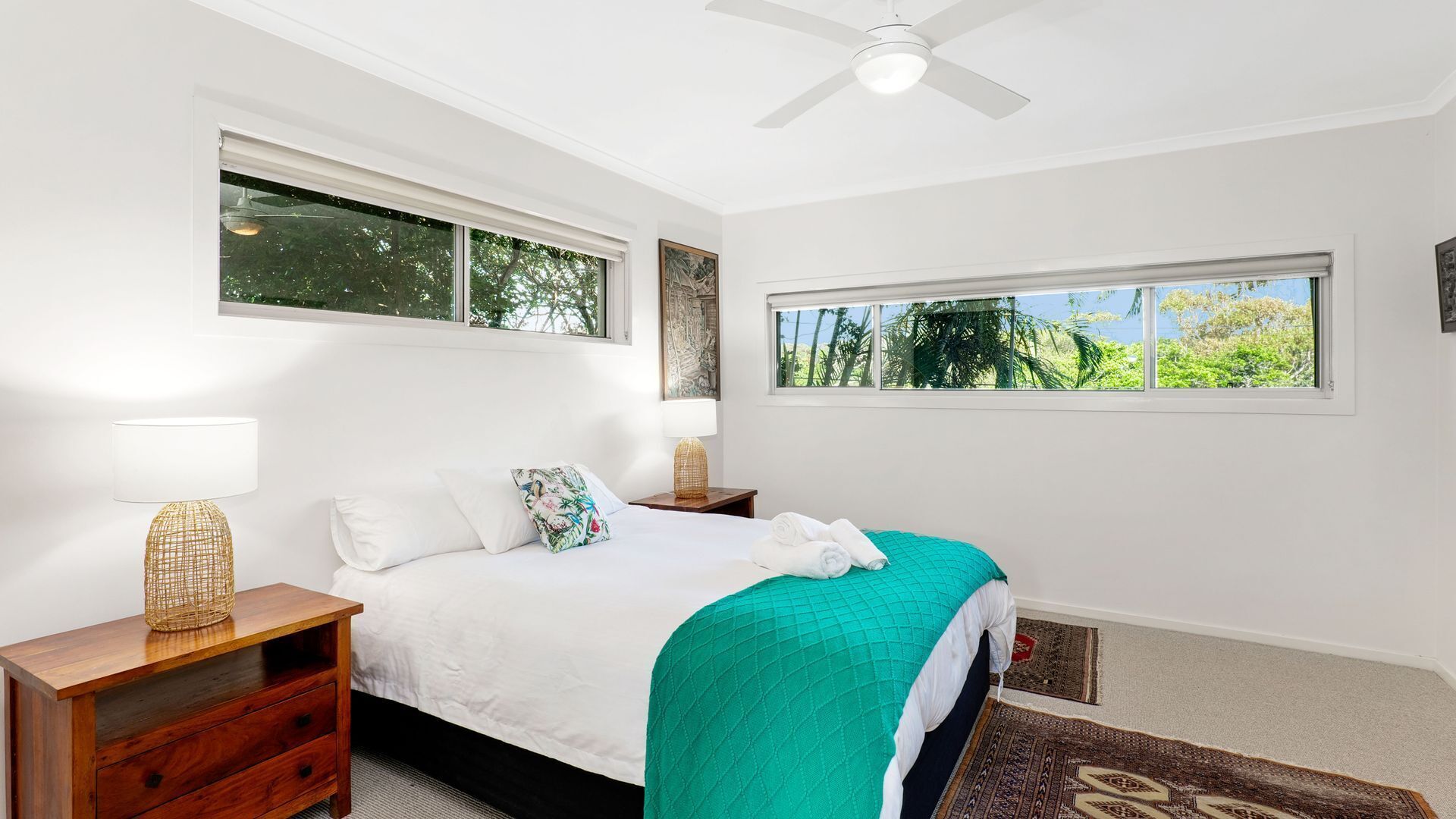 Camera da letto con un letto, due comodini, una ventola a soffitto e ampie finestre con vista sul verde.