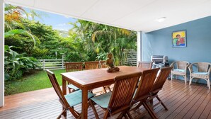 A wooden deck with a table and chairs, a Buddha statue, a grill, wicker chairs, and a blue wall with a painting. - Welcome to "Buddha Beach House," the perfect beach retreat in coastal haven Sawtell. (Sawtell)