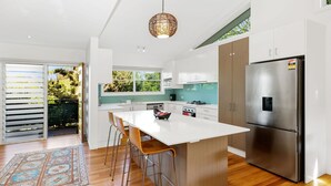 A modern kitchen with a large island, stainless steel appliances, and a view to the outdoors. - Welcome to "Buddha Beach House," the perfect beach retreat in coastal haven Sawtell. (Sawtell)