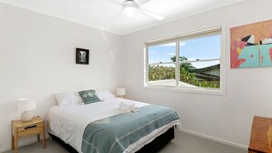 A bedroom with a bed, a nightstand, a window with a view, and a painting on the wall. - Welcome to "Buddha Beach House," the perfect beach retreat in coastal haven Sawtell. (Sawtell)