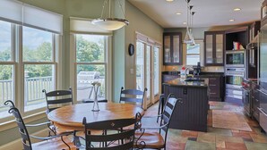 A kitchen with a central island, large windows, and a dining area with chairs. - The Hanger House on Lake Norman Airpark (Mooresville)
