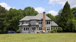 A two-story house with a large front porch, a chimney, and a well-maintained lawn. - The Hanger House on Lake Norman Airpark (Mooresville)