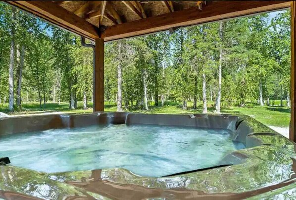 A hot tub under a wooden pergola with a forest view.