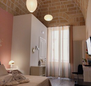A bedroom with a bed, a desk, a chair, a window with curtains, and a radiator. - Antica Dimora Le sette Lune (Altamura)