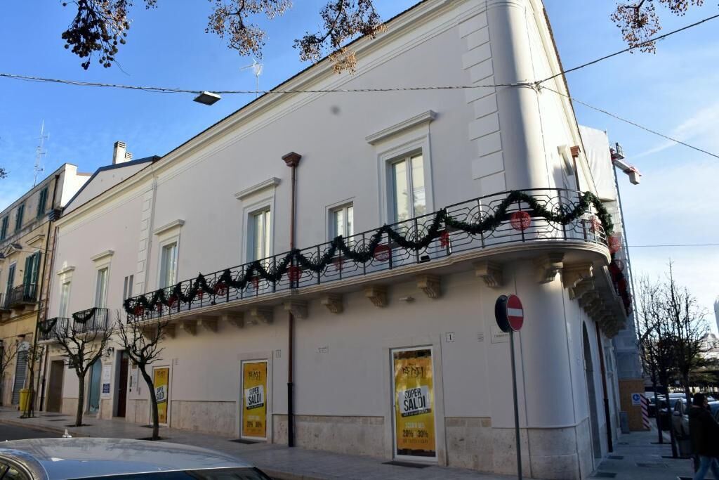 A corner building with a white facade, a balcony with black railings, and two yellow sale signs.