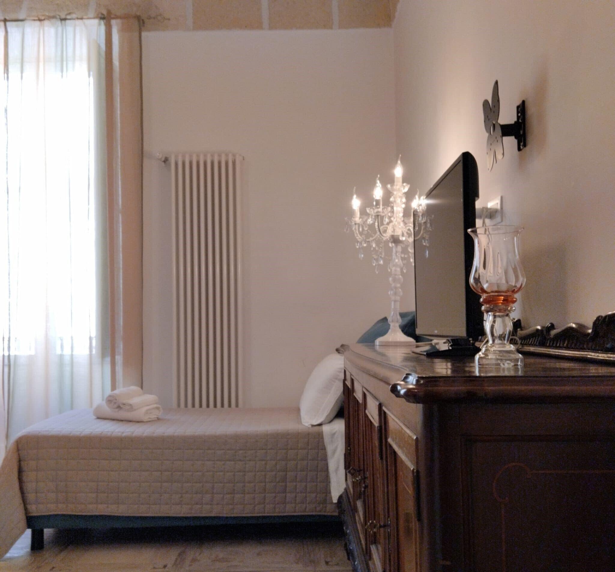 A bedroom with a bed, a dresser, a mirror, a chandelier, and a radiator.
