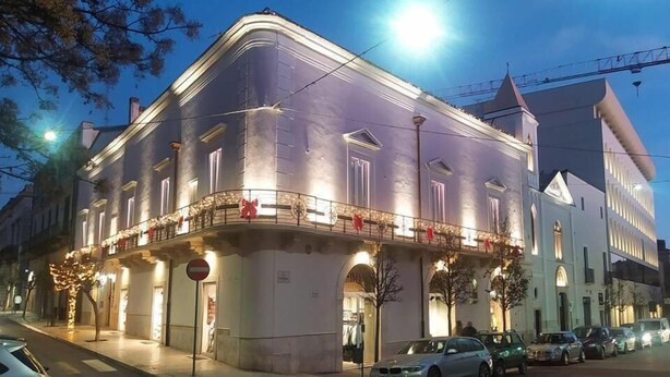 Un edificio histórico con un balcón adornado con lazos rojos, una señal de prohibido el paso y coches estacionados.